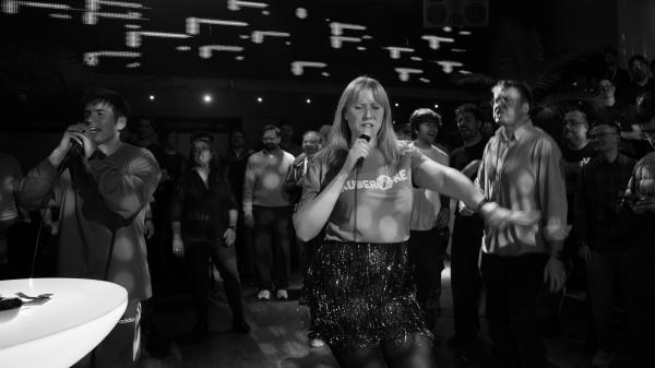 Woman in Kuberoke shirt is standing in the center, singing into a microphone